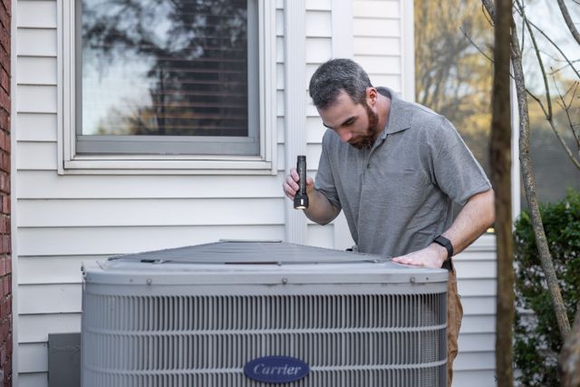 person looking at an hvac unit with a flashlight